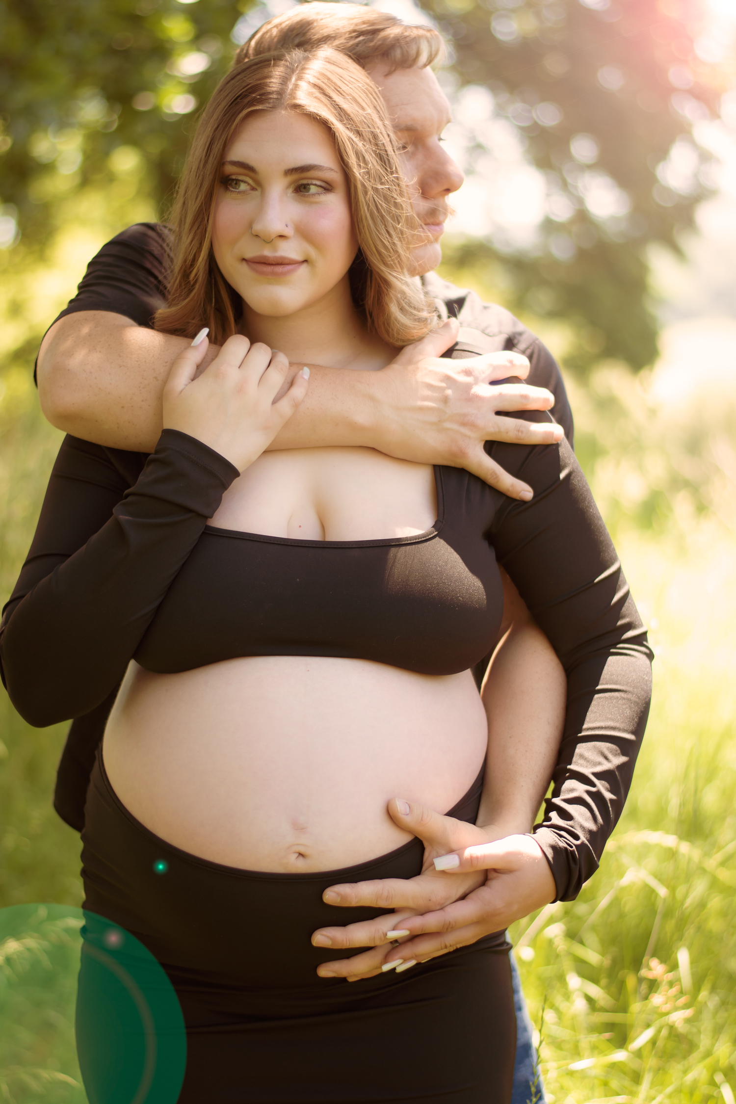 Romantic maternity portraits captured outdoors with soft natural lighting and green foliage.