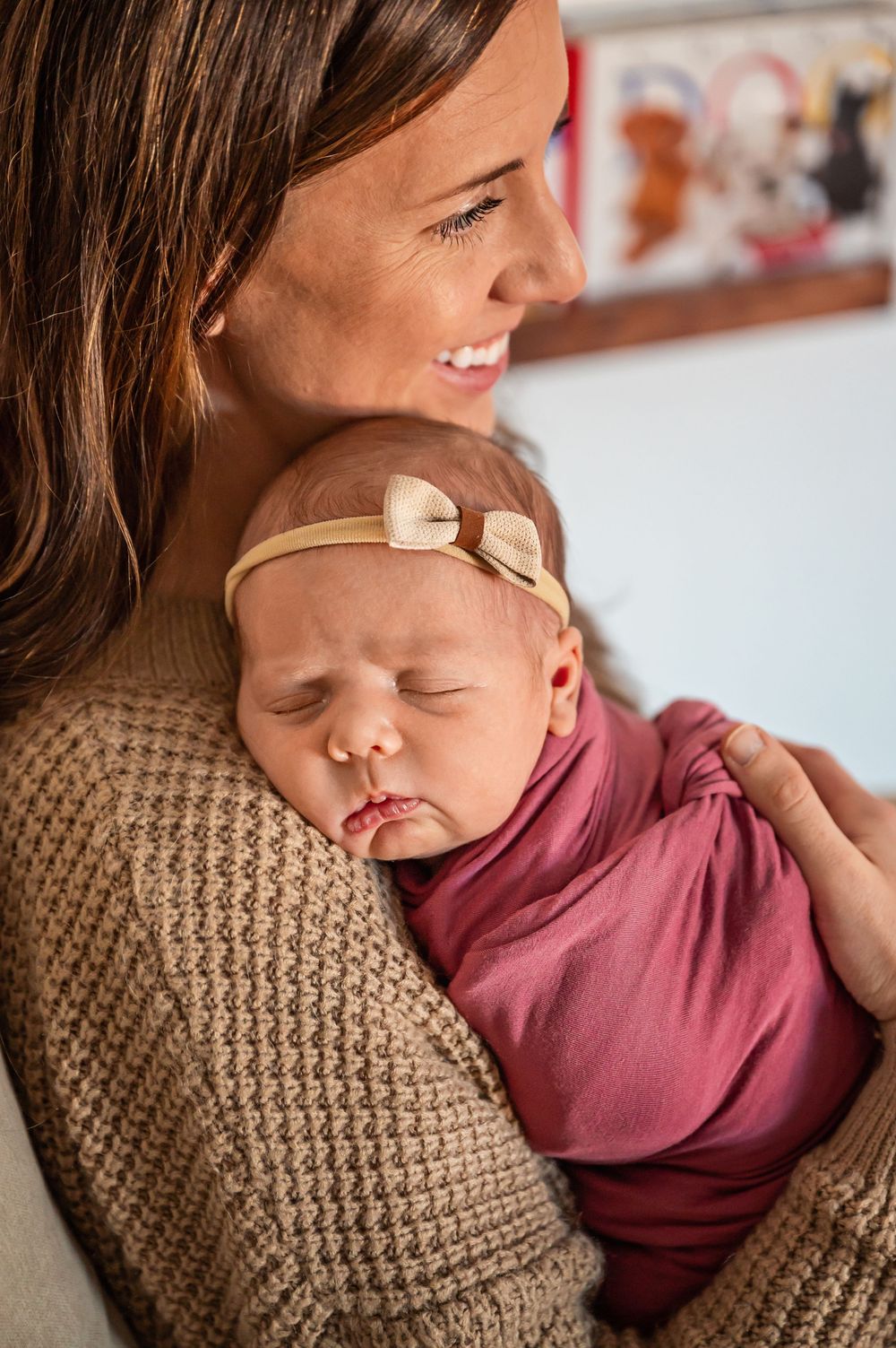 A sleeping baby in a burgundy onesie rests peacefully against a knitted brown blanket.