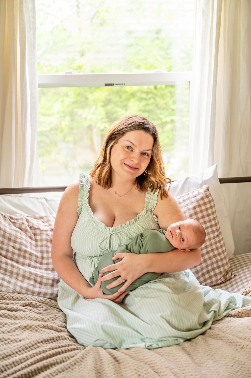 A parent and baby in matching mint green outfits share tender moments on a gingham blanket in a sunlit room.
