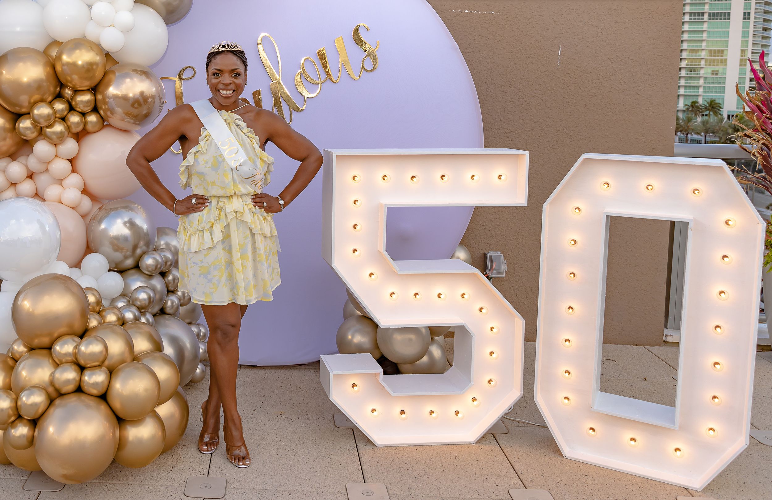 A celebration setup features illuminated number 50 signs with gold balloon decorations against a neutral backdrop.