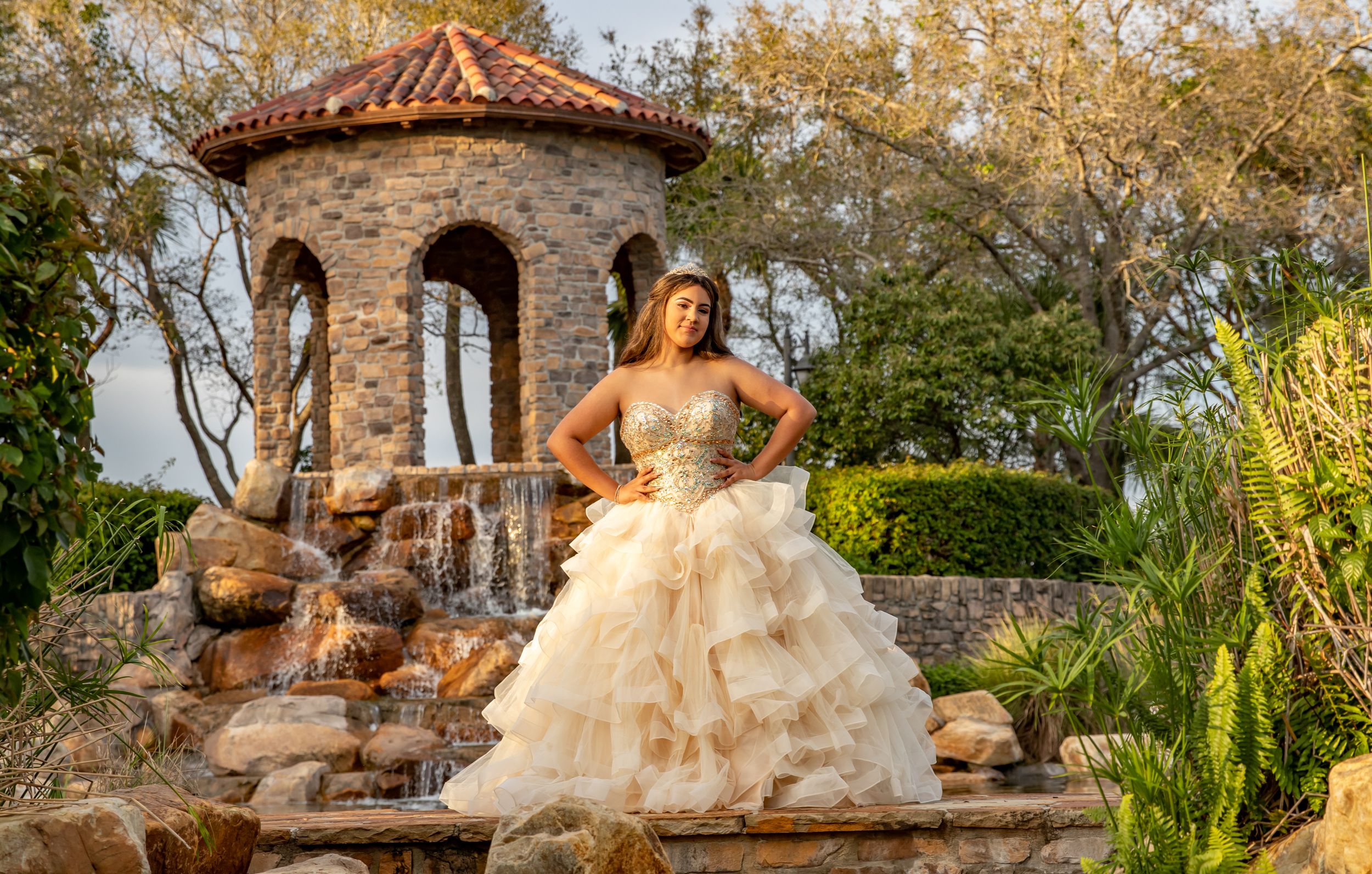 Ornate cream colored ballgown photographed at stone gazebo in garden setting.