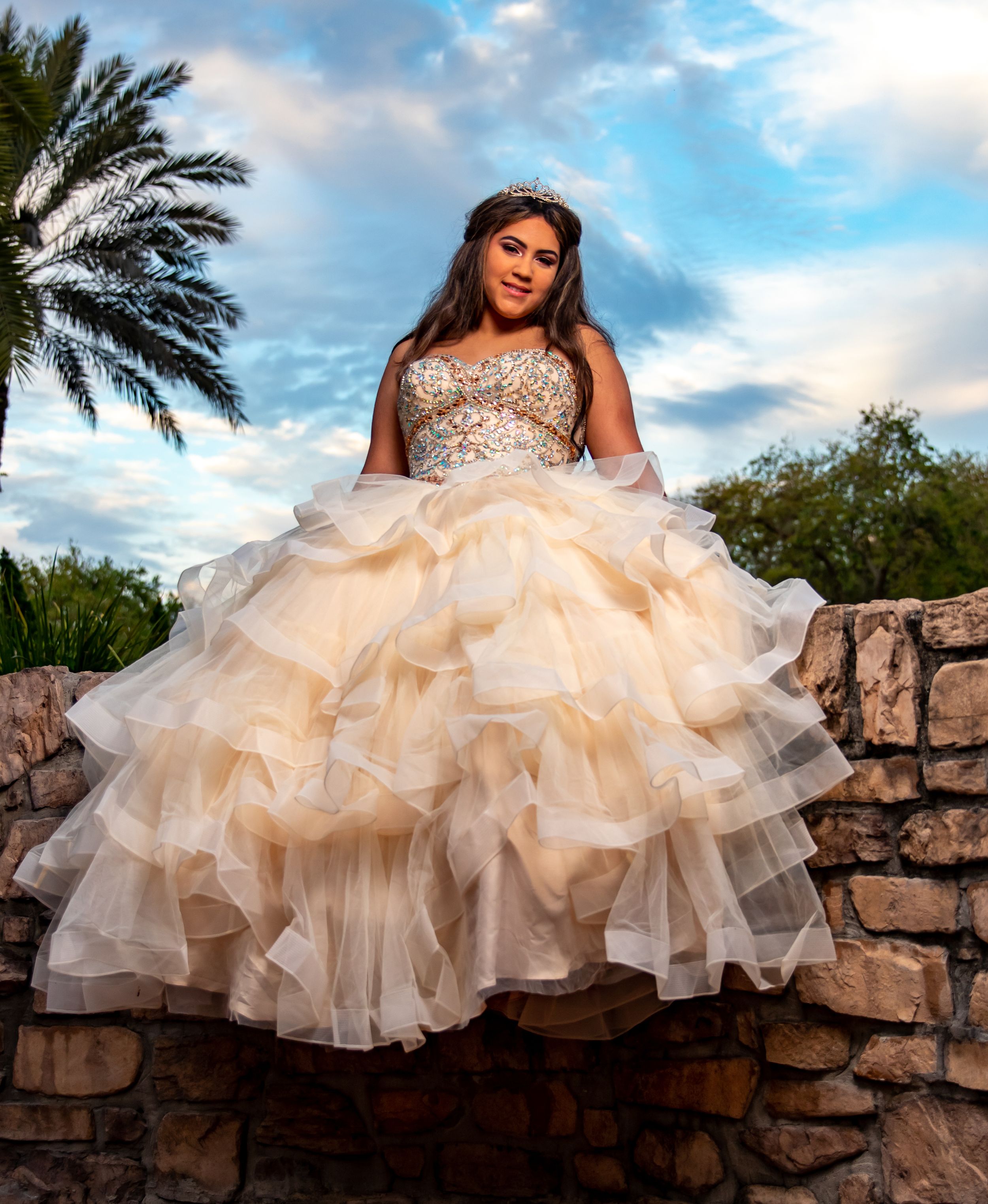 Elegant quinceañera dress with sparkly bodice and ruffled cream tulle skirt against sunset sky and palm trees.
