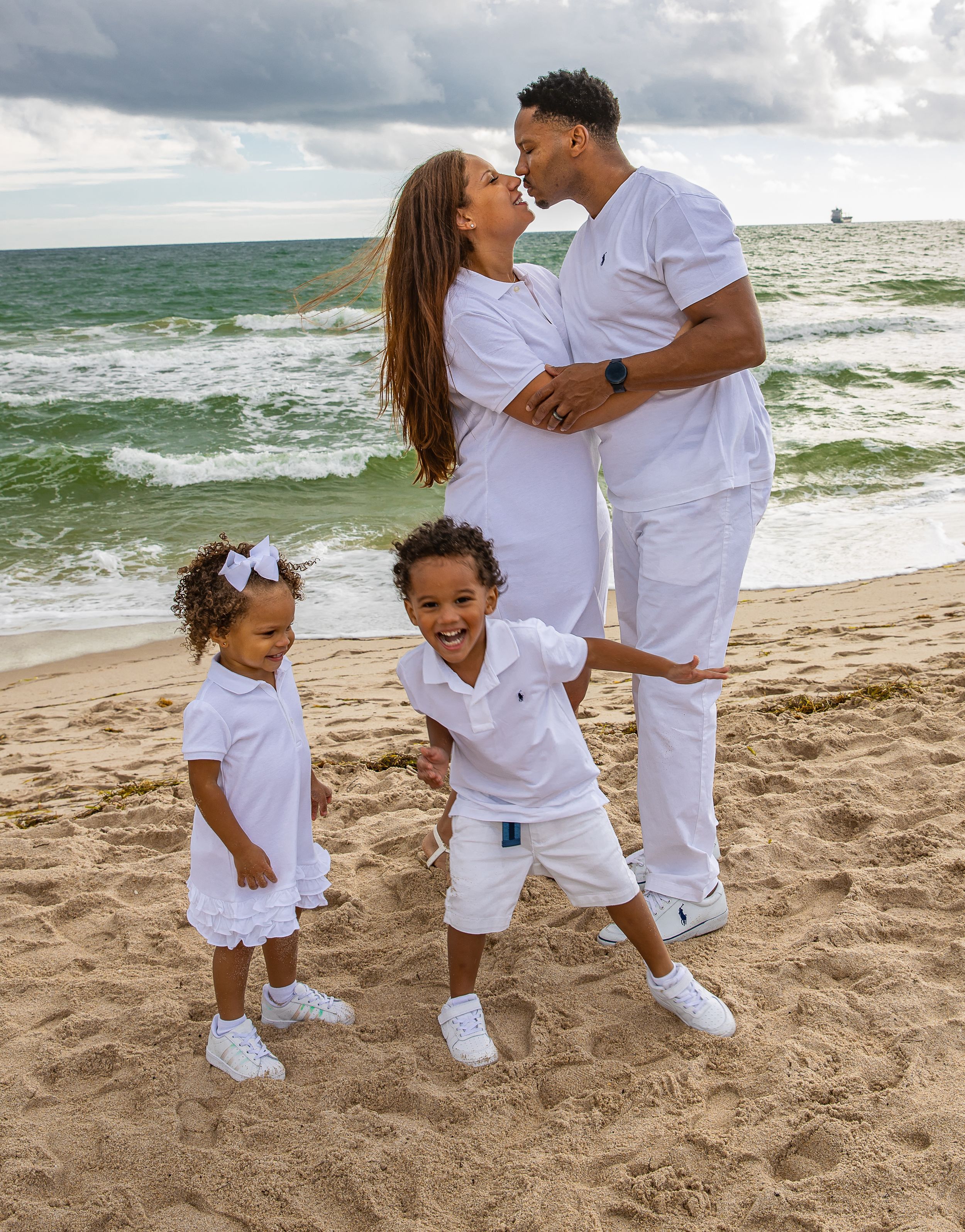 Family in matching white outfits playing together on sunny beach.
