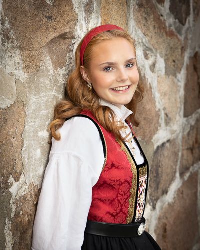 Traditional Norwegian folk costume shown in a series of portrait photos against a rustic stone wall background.