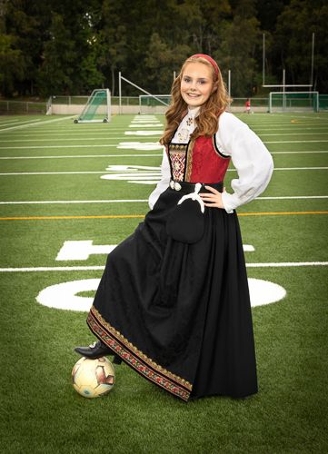A person in traditional Norwegian dress poses with a soccer ball on a football field in a creative photo series.