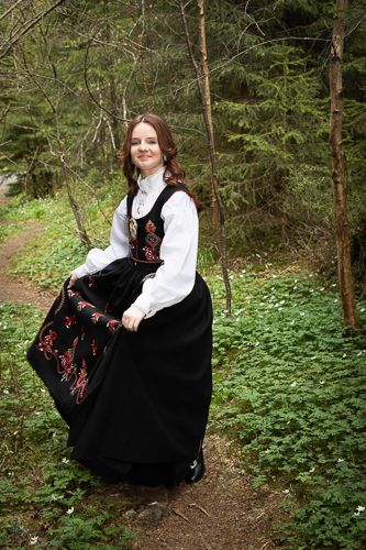 A girl wearing a traditional black and white folk dress sits on a forest path surrounded by lush greenery.