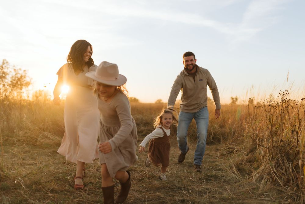 Joyful family moment captured while running through a sun-drenched field at golden hour.