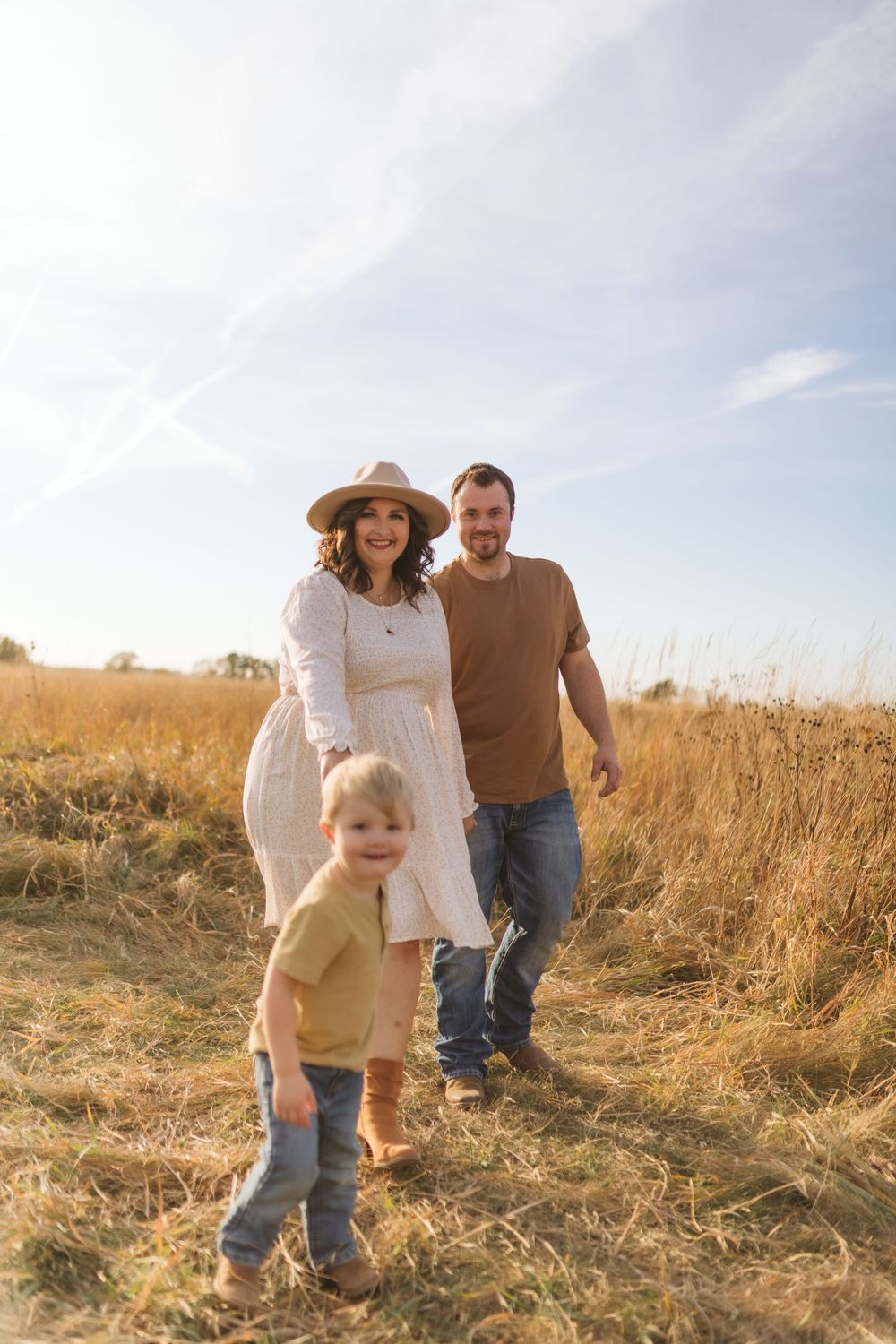 Family walking together on trail through golden autumn field.