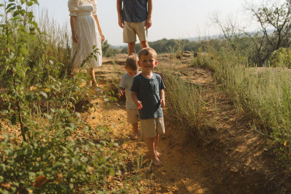 A group hiking along a dirt trail through tall grass and bushes on a sunny day.