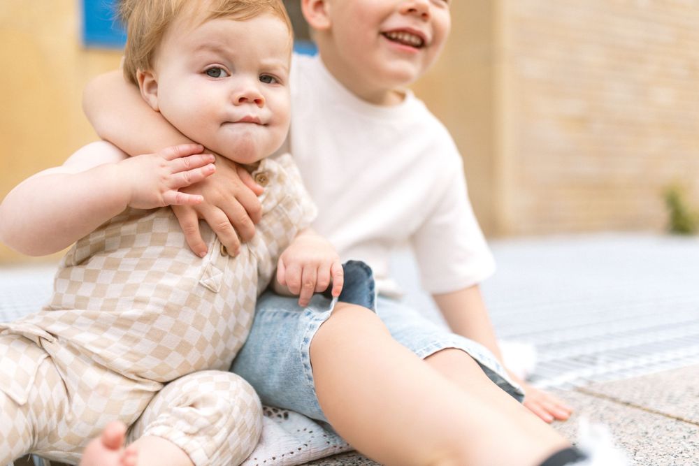 Two children sharing joyful moment together on light colored surface.