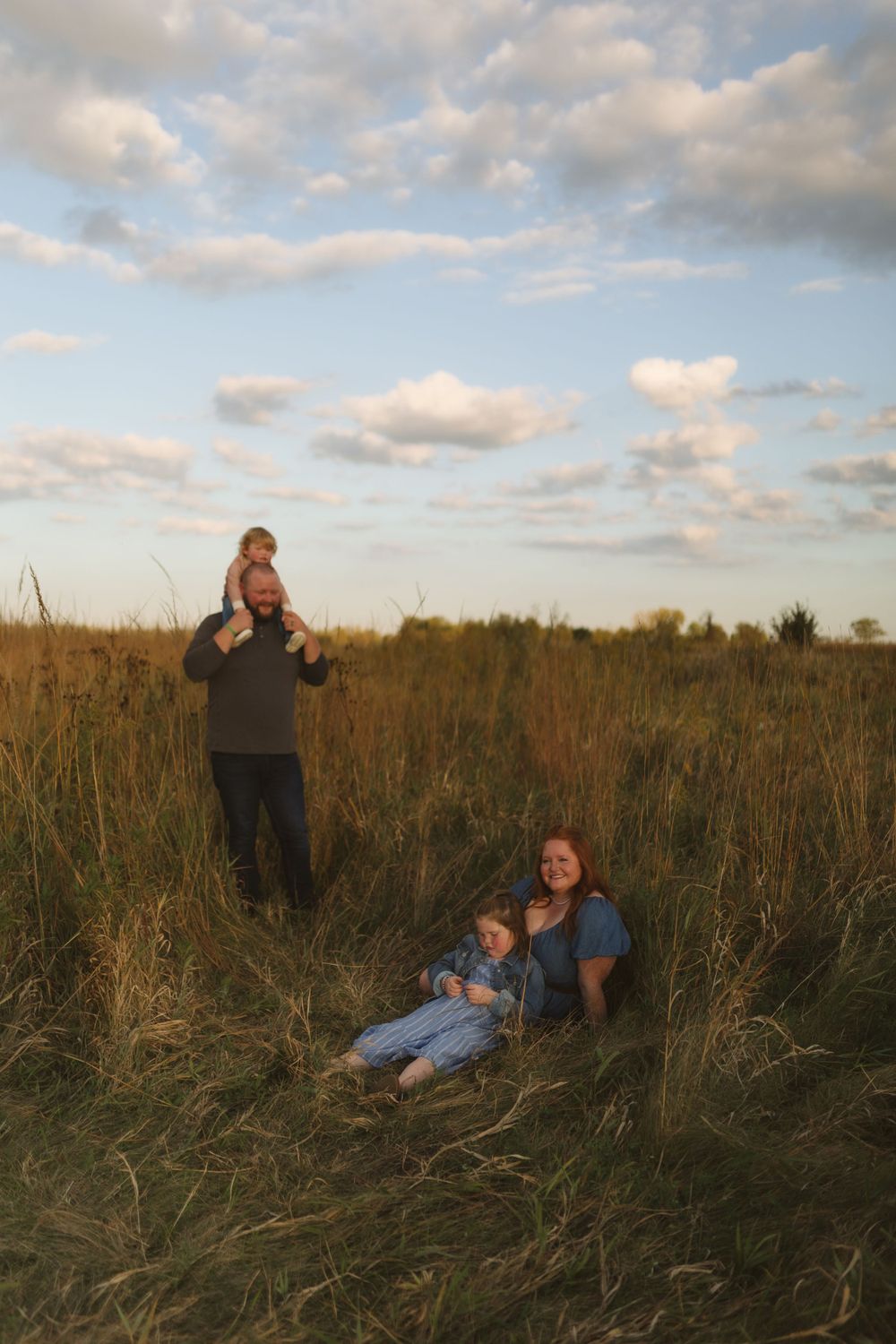 People gathered in a tall grass field during golden hour with cloudy sky above.