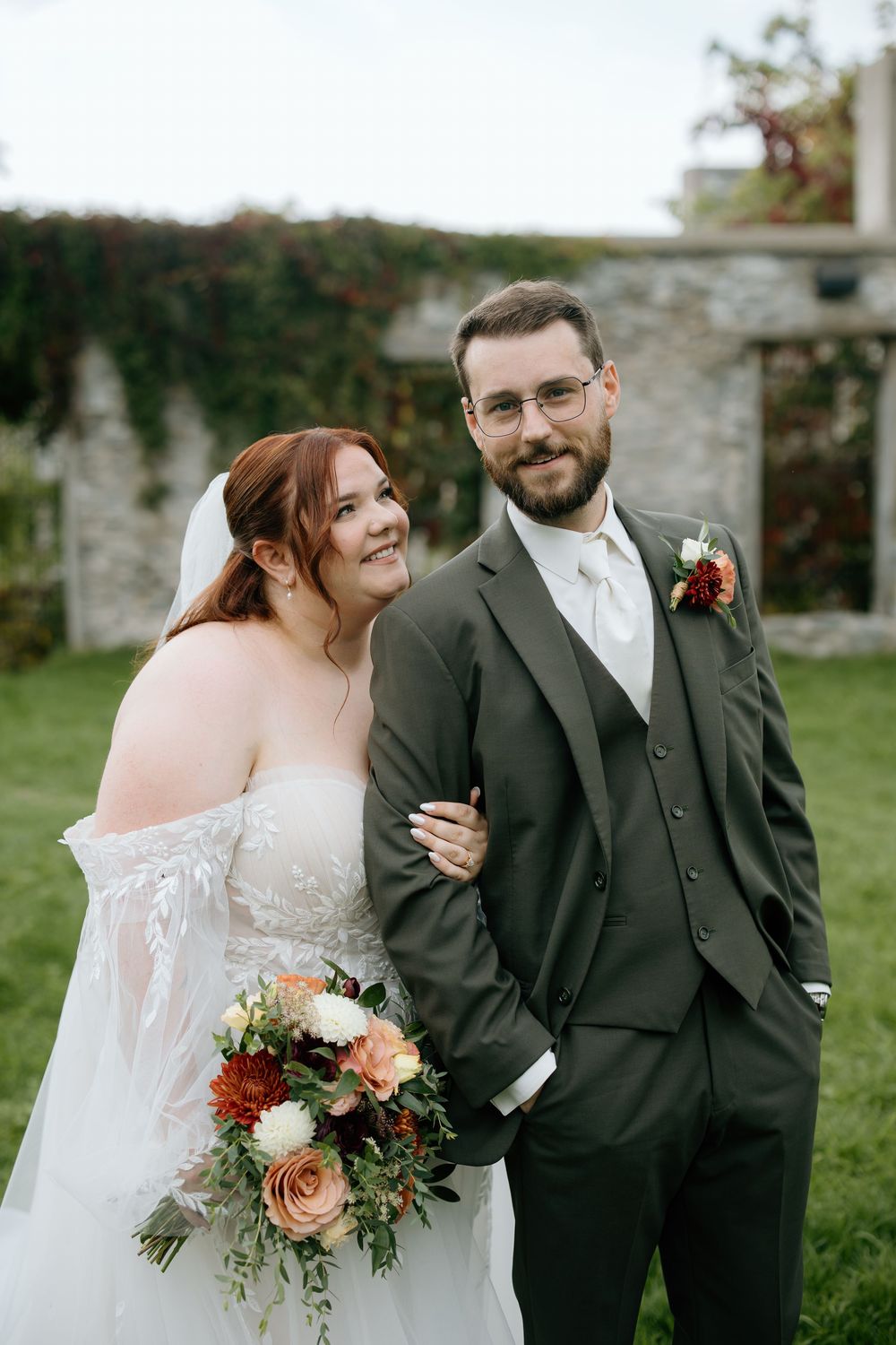 A happy couple shares joyful moments together outdoors during their wedding celebration with autumn-toned floral bouquet.