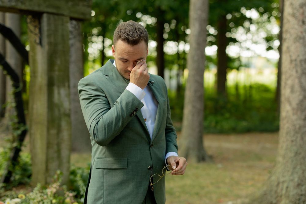 A person in a green suit wipes tears from their eyes while standing in a wooded outdoor setting.