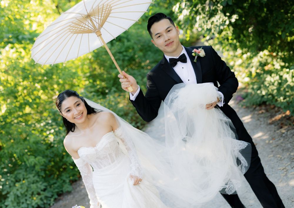 A romantic wedding couple poses with white parasols in a lush garden setting during their outdoor photo session.