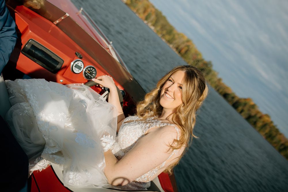 A bride in a white wedding dress poses playfully with cotton candy against a waterfront backdrop.