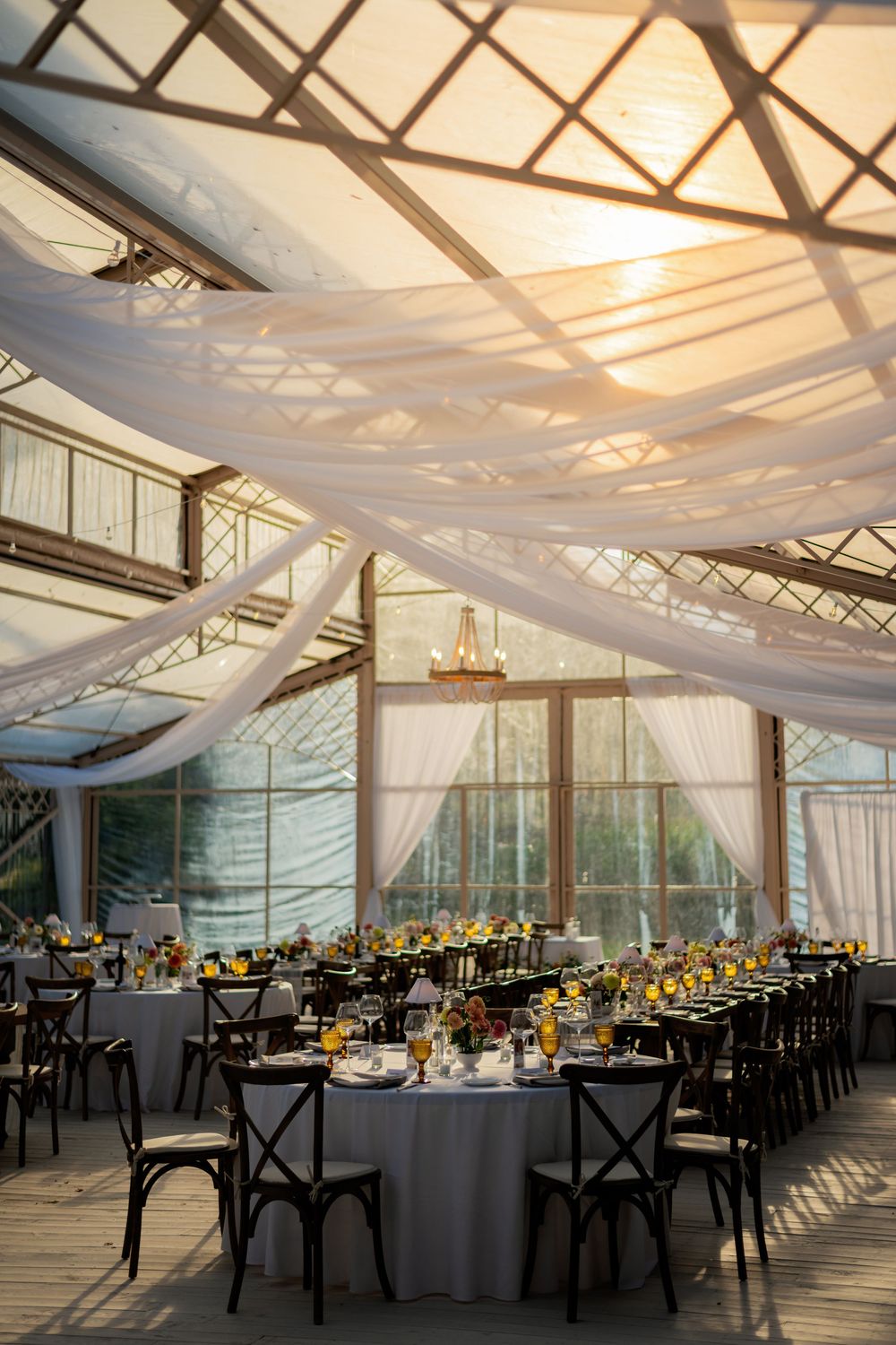 Elegant wedding reception venue with draped white fabric ceiling and black cross-back chairs at round tables.