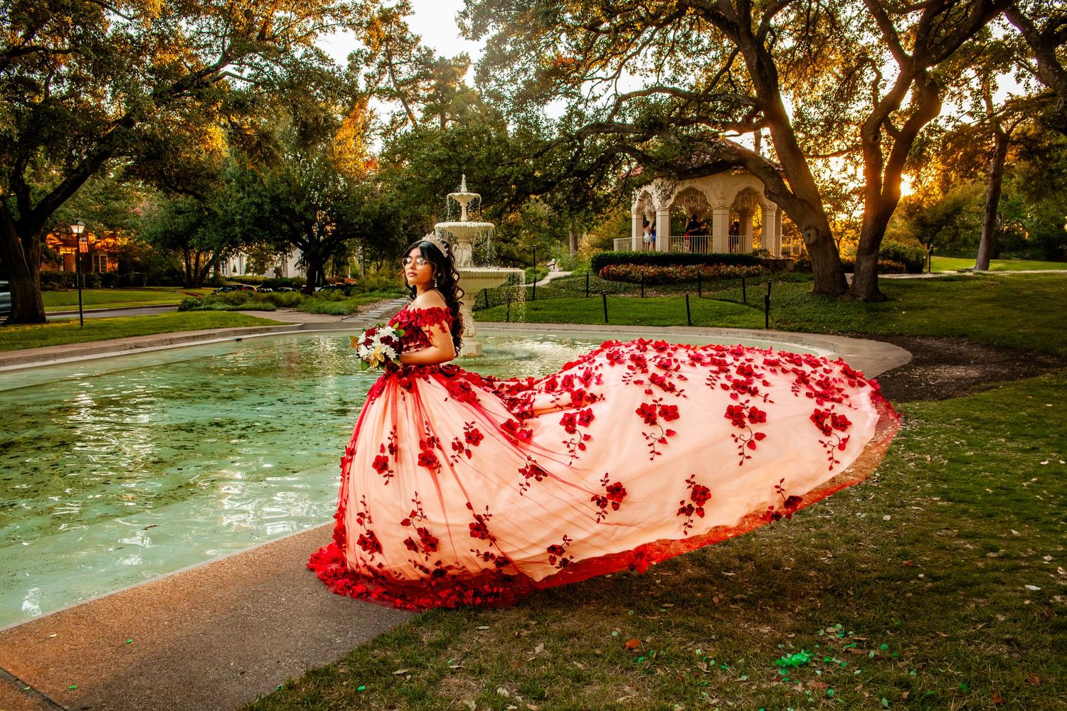 Panoramic view of flowing red dress train spread across autumn park landscape at sunset.