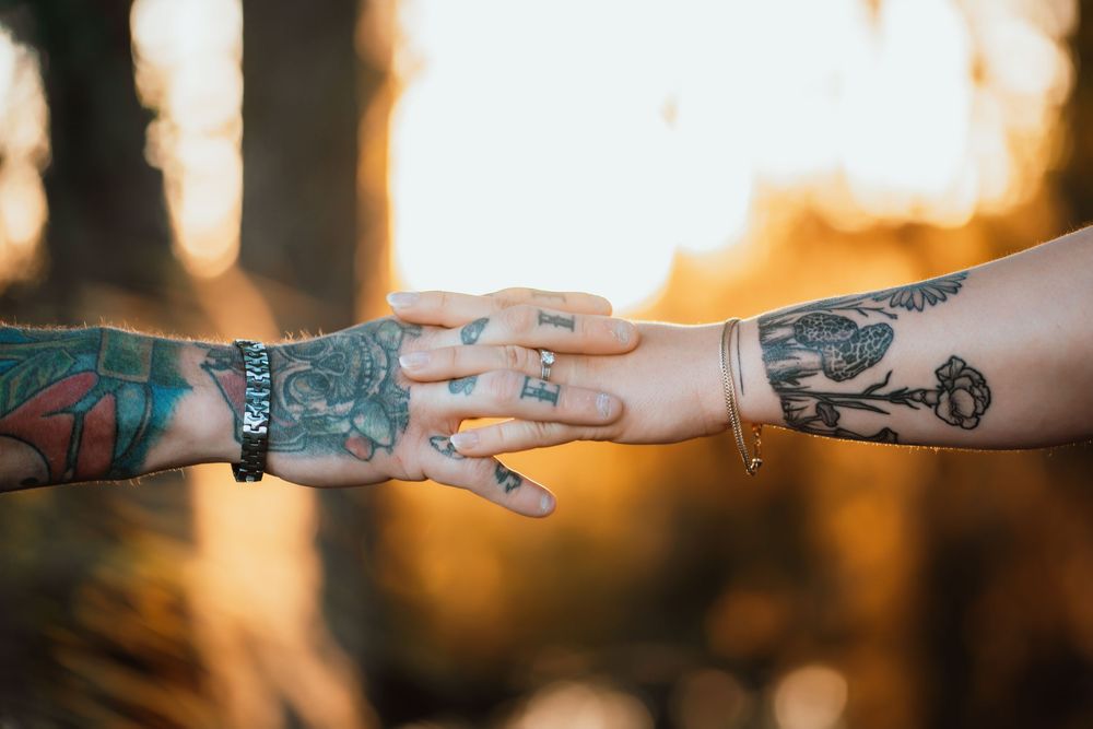 holding hands in front of a sunset, tattoos, engagement ring