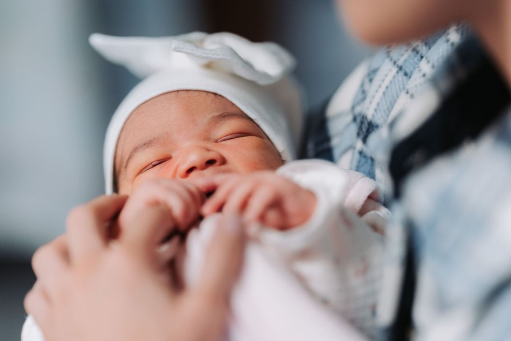 A newborn baby wrapped in a white cloth smiles contentedly while being held.