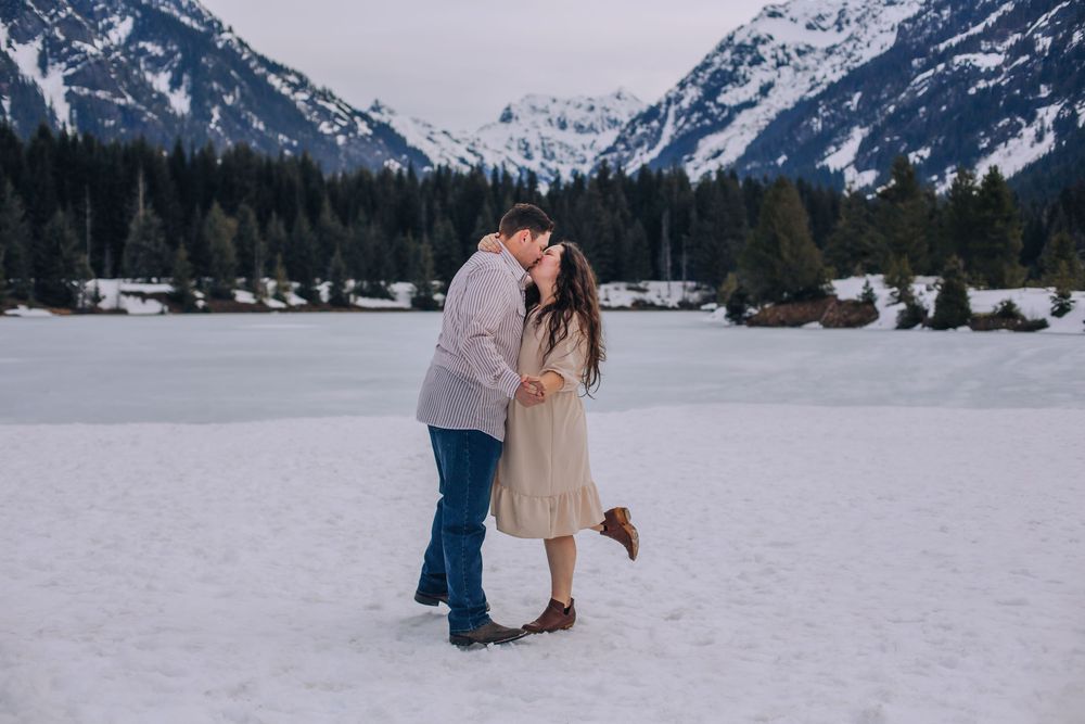 Romantic winter engagement photos on a snow-covered lake with mountains in background. Spokane Liberty Lake Photographer Family Photographer