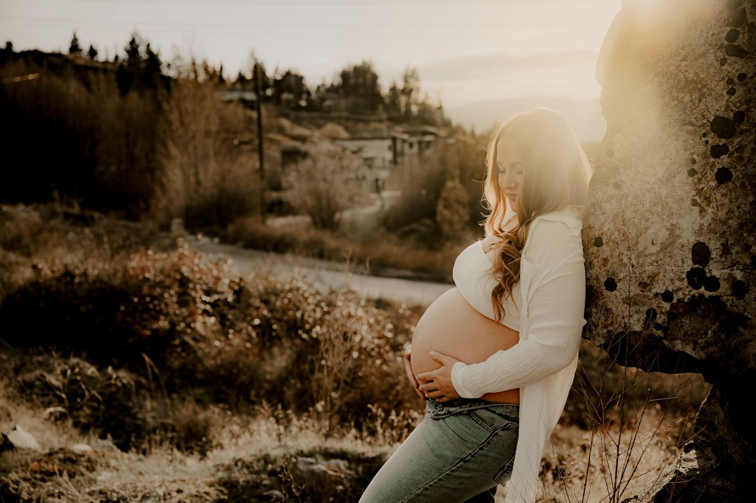 Silhouetted maternity photo at golden hour in mountain landscape.