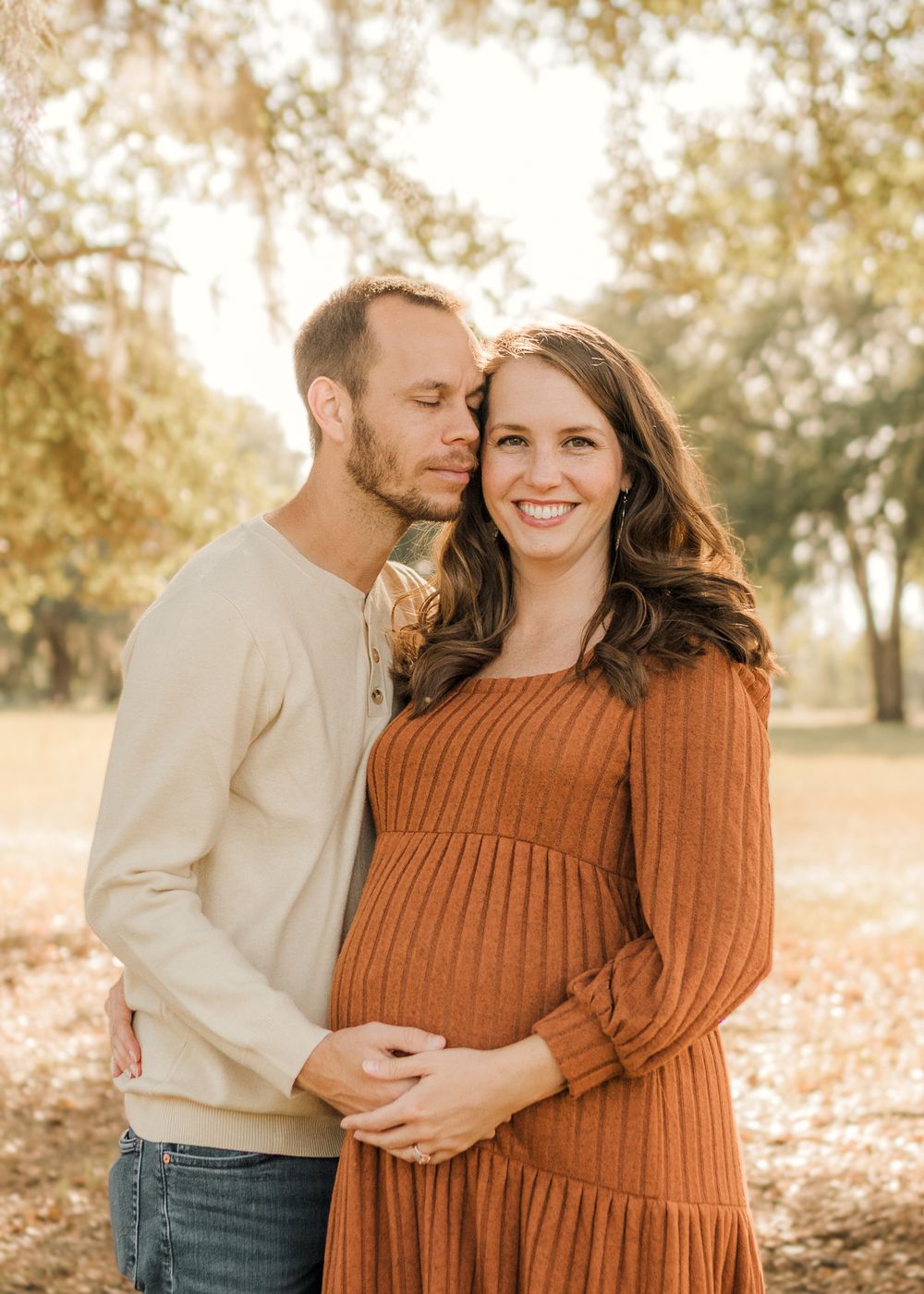 A couple embraces in a romantic autumn setting with fallen leaves and warm lighting in the background.