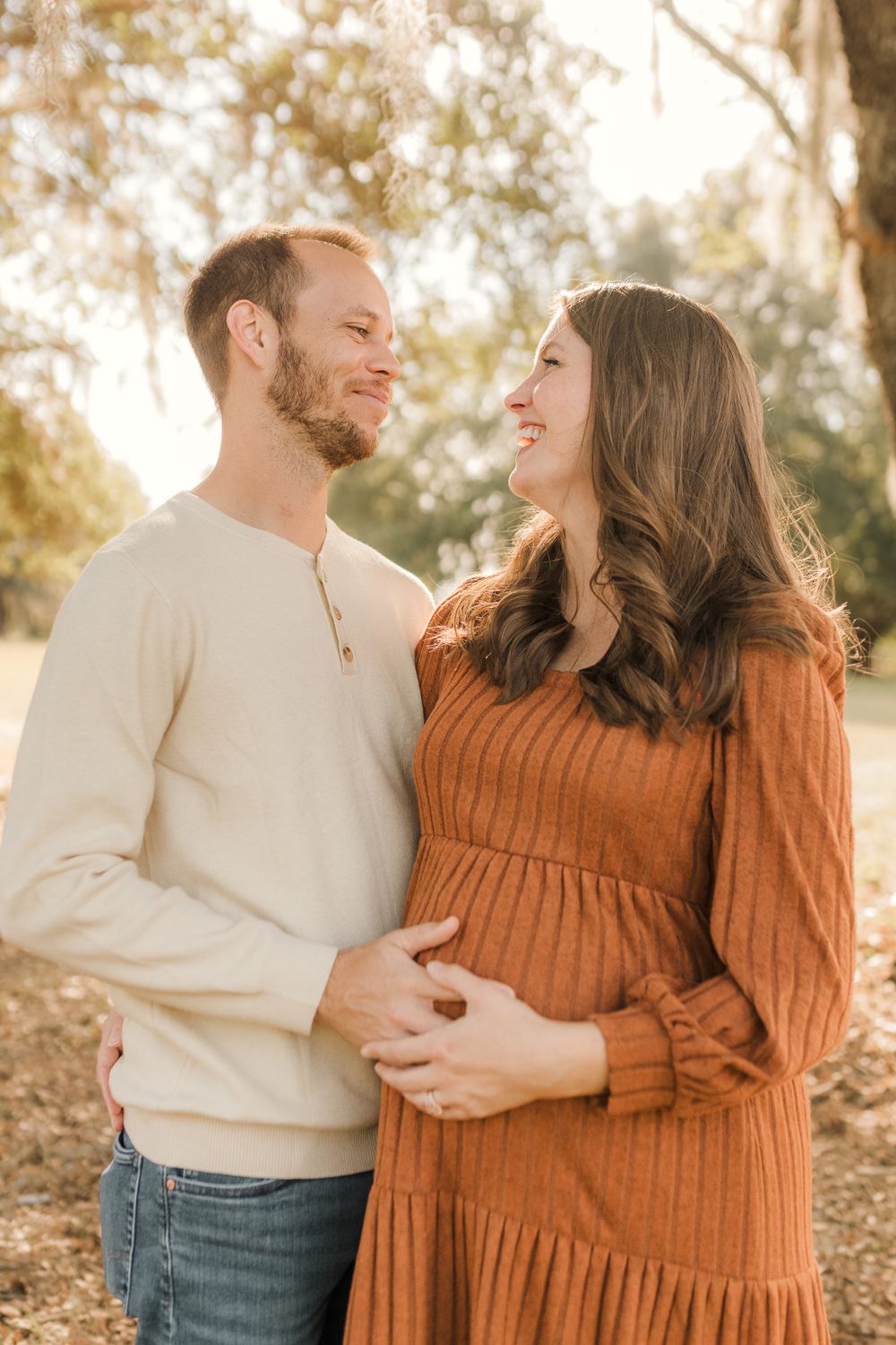 Couple in casual fall attire sharing intimate moments during golden hour maternity photoshoot outdoors.