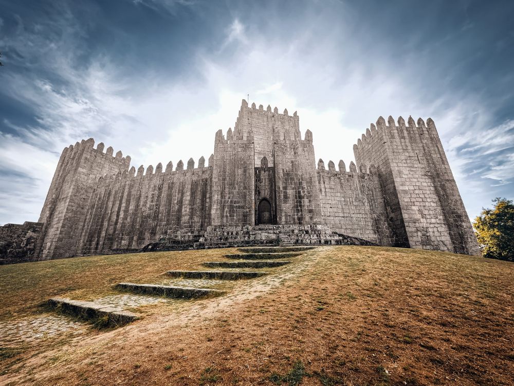 Medieval stone castle with crenellated towers under dramatic cloudy sky.