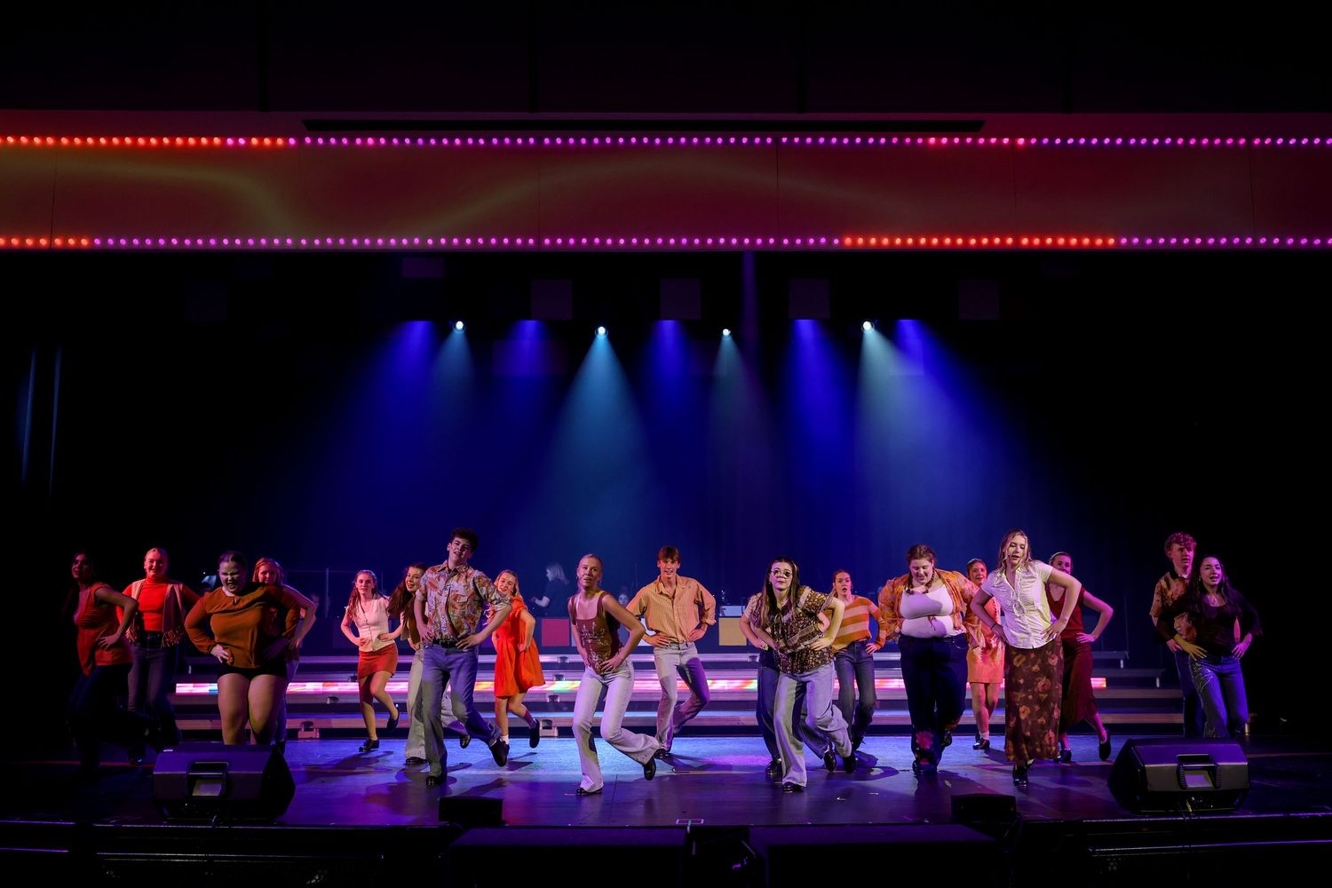 Dancers perform an energetic group number with dramatic blue stage lighting in a theatrical production. Theatre photography.
