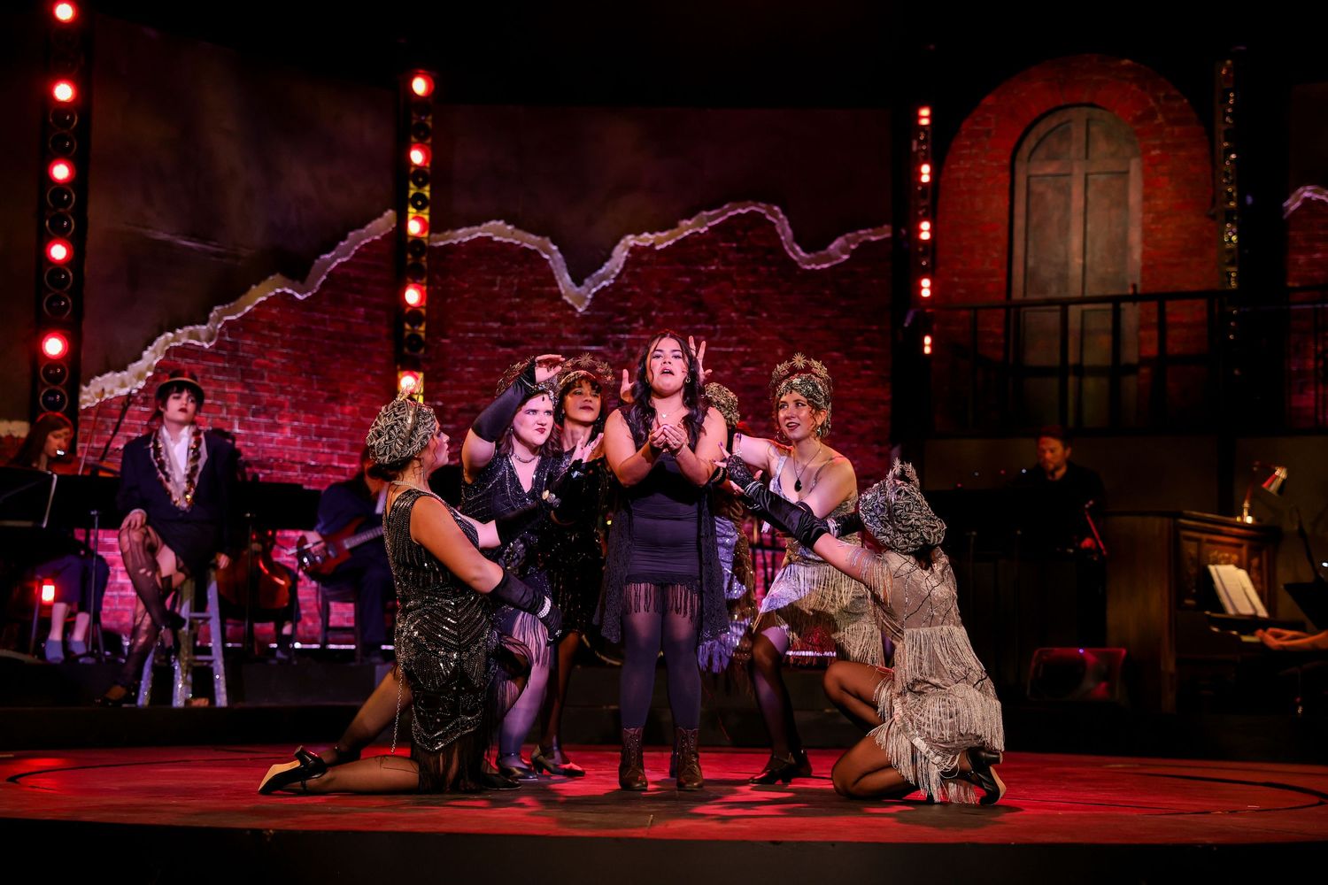 Theatrical performers act in dramatic scenes on a dimly lit stage with red lighting effects and atmospheric set pieces. Theatre photography.