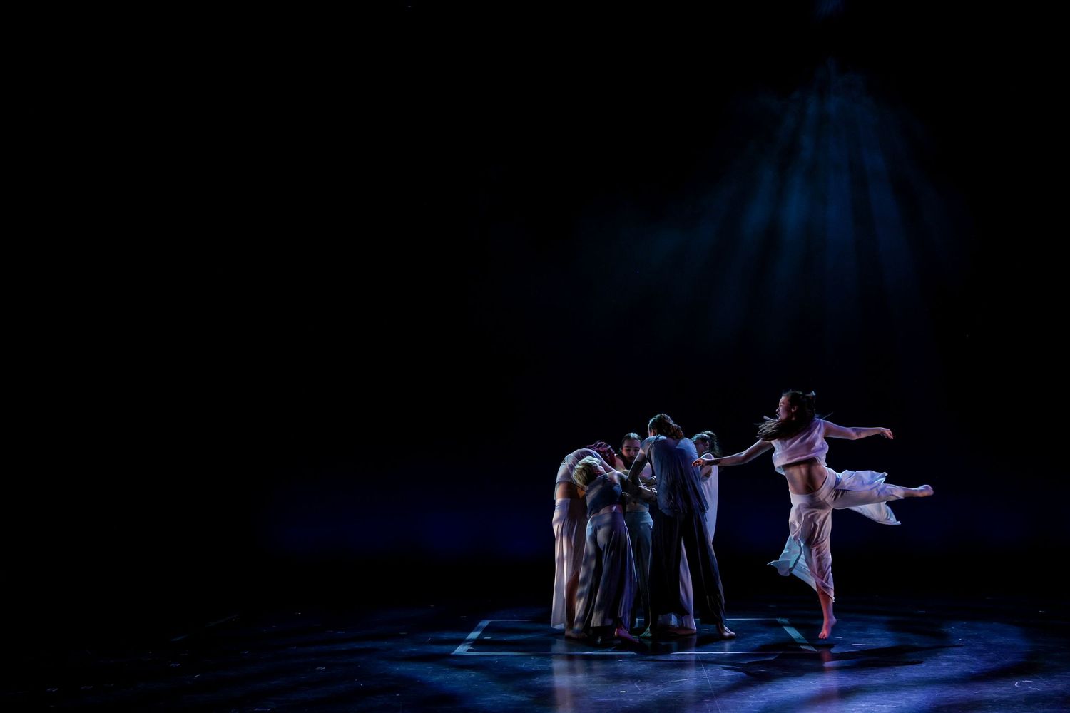 Dancers perform in dramatic lighting on a dark stage with a blue spotlight creating an ethereal atmosphere. Theatre photography.