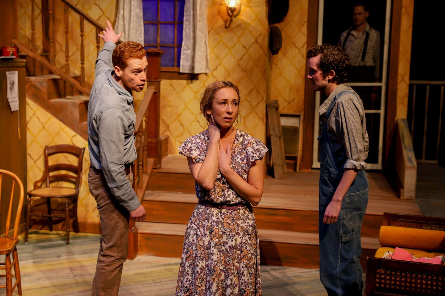 Three performers on stage in a period-style production with warm lighting and rustic interior set design.