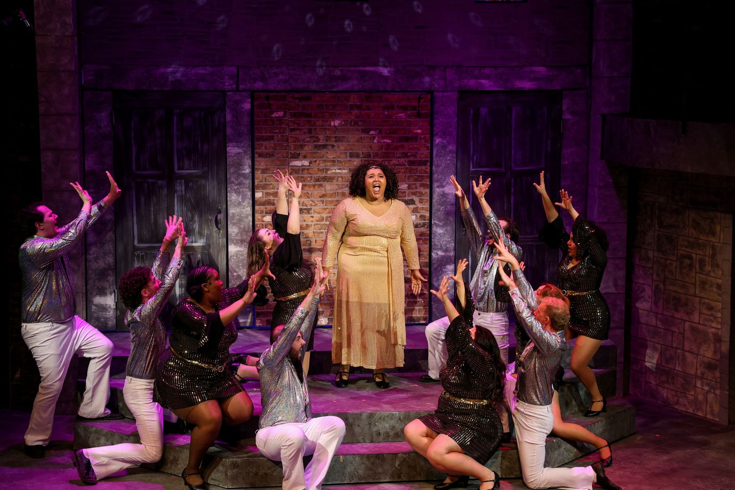 Theatrical performers in the midst of an energetic choreographed dance number on stage with dramatic purple lighting. Theatre photography.