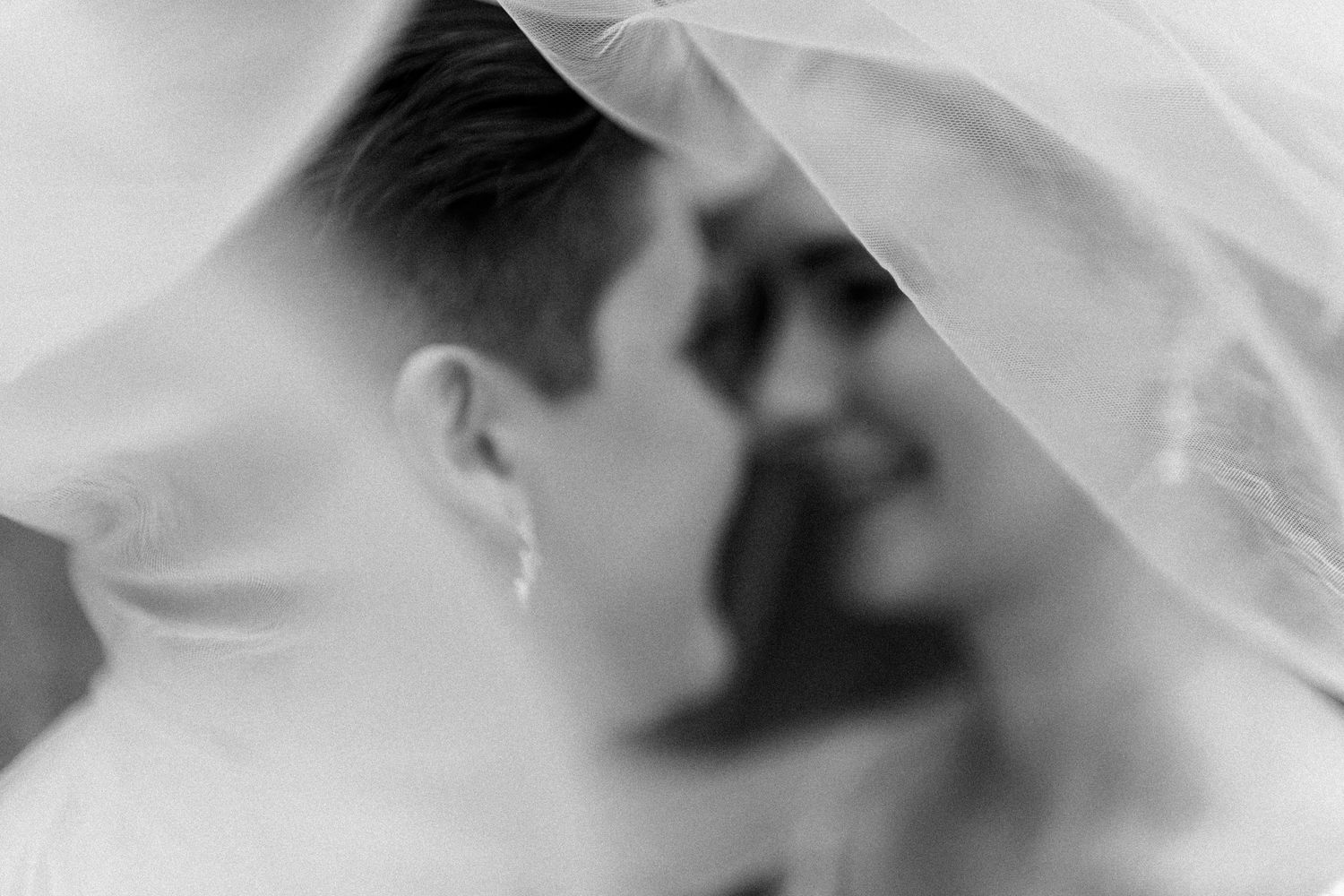 A romantic black and white wedding photo showing a couple's intimate moment under a flowing veil.