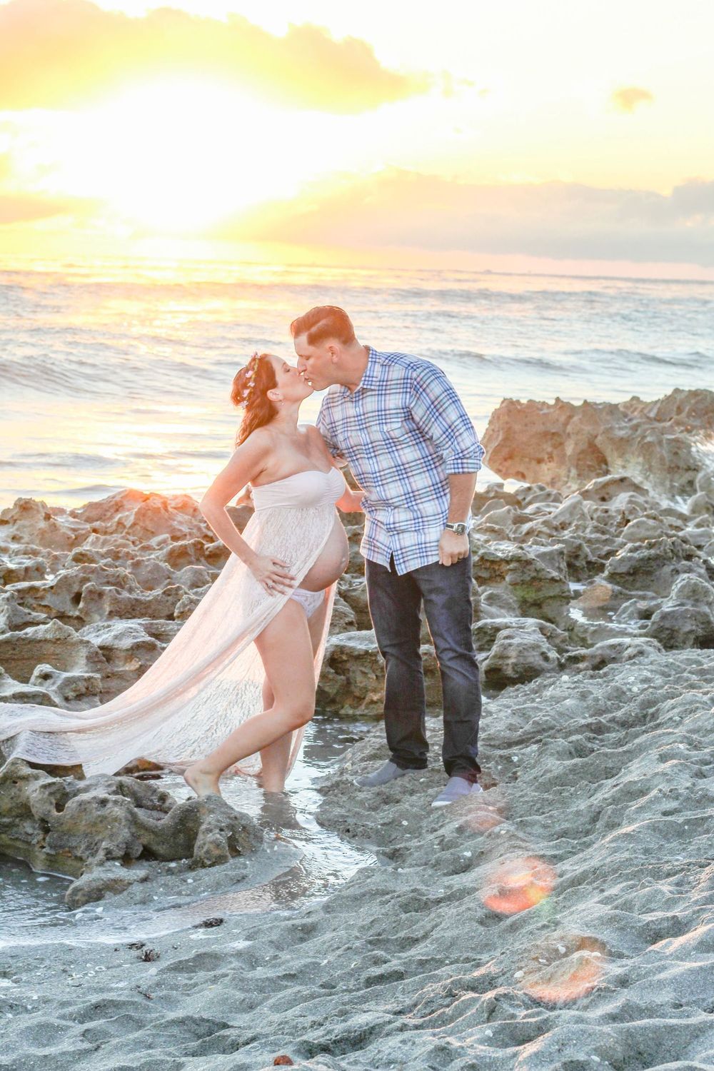 Pregnant couple shares a kiss on rocky beach at golden sunset at blowing rocks beach Jupiter fl.