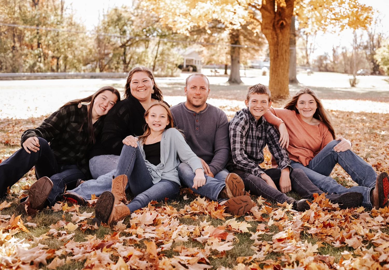 Family group sitting together on fallen autumn leaves under tree.