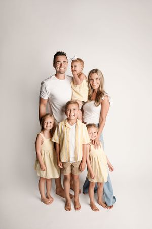 Happy family of seven with parents and five children posing together against a white studio background.