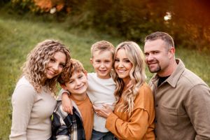 Happy family of five with two boys posing outdoors in fall foliage during golden hour session.