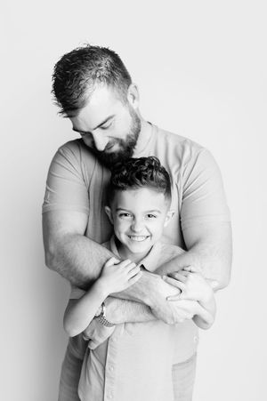 A black and white portrait of a bearded father hugging his smiling young son warmly.