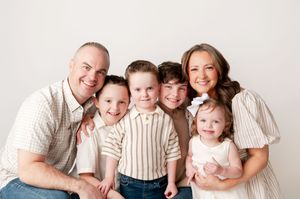 A happy family of six with four young children smiles together in a bright white studio.