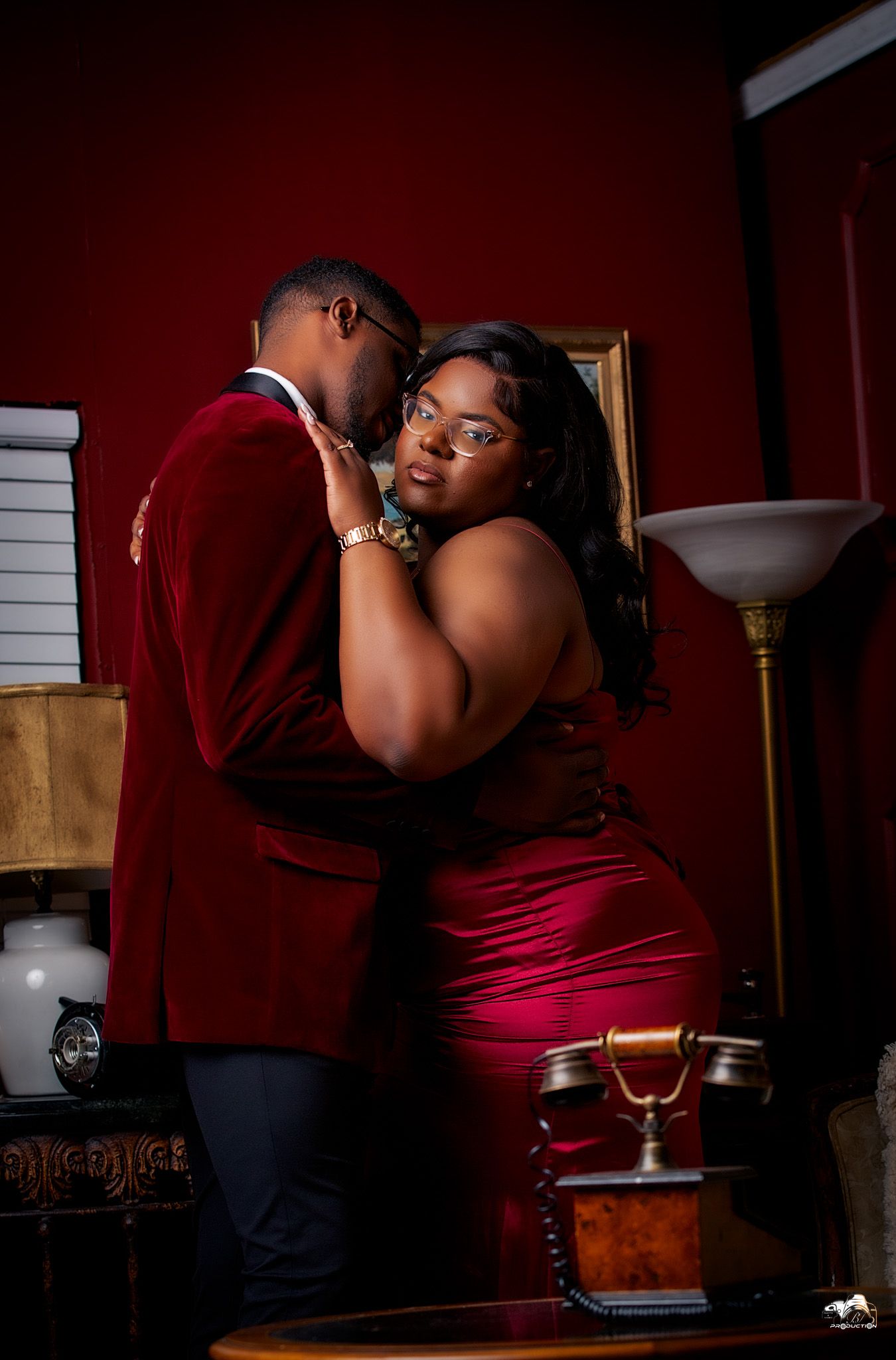 Romantic couple in red formal wear embrace in dimly lit elegant setting.