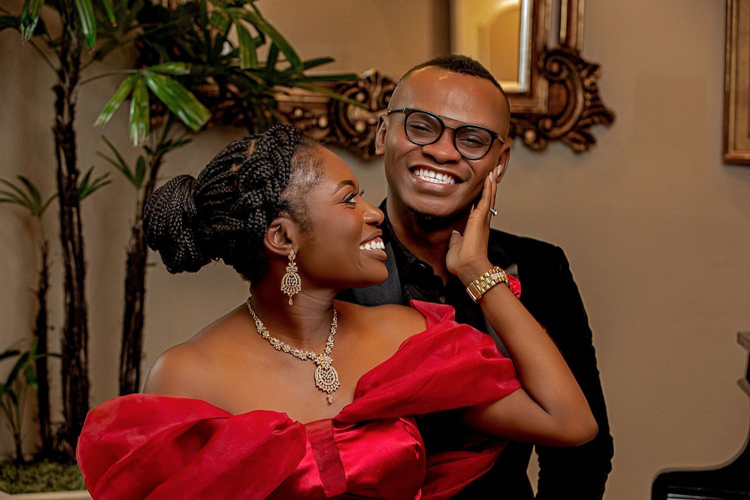A couple shares an intimate moment in formal evening wear against an elegant interior backdrop.