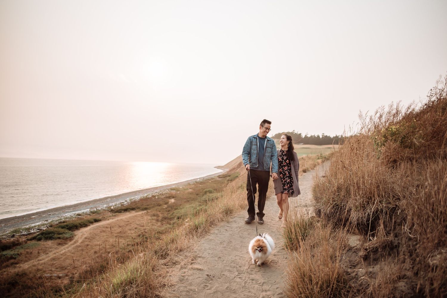 Couple walking dog along coastal path at sunset with ocean views.