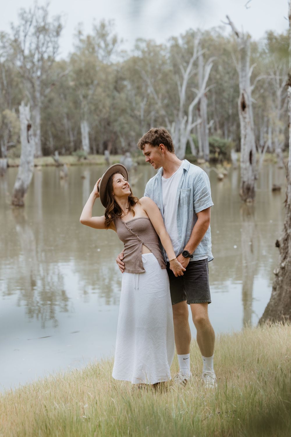 A couple shares romantic moments by a serene lake with gum trees reflected in the still waters.