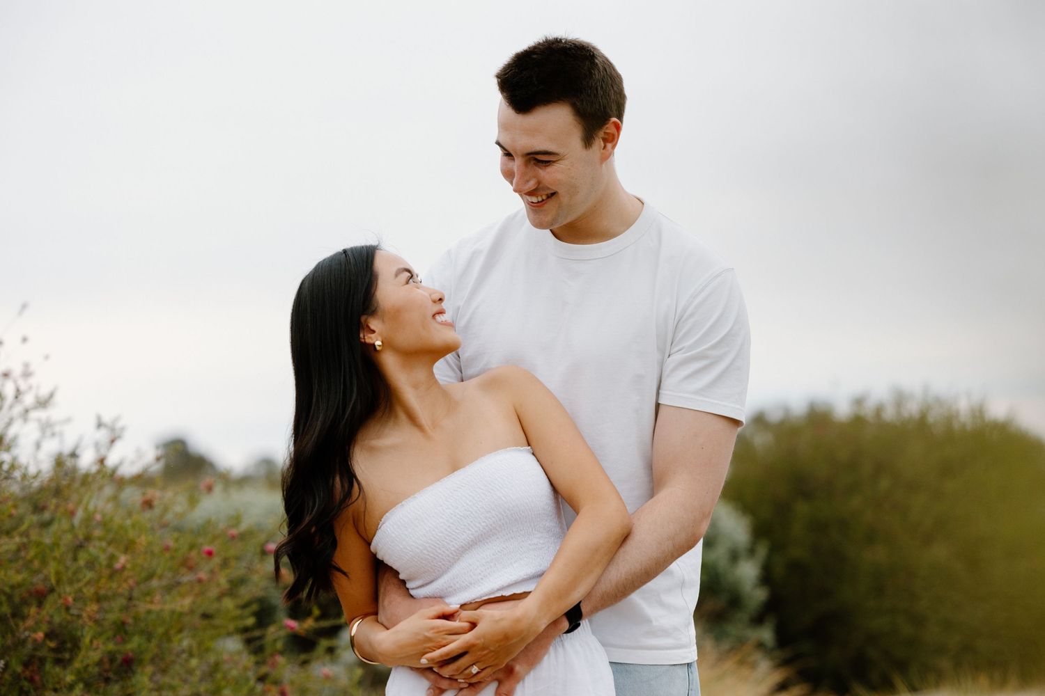 A couple in white outfits share tender moments together during an outdoor photoshoot in a natural setting. location shepparton