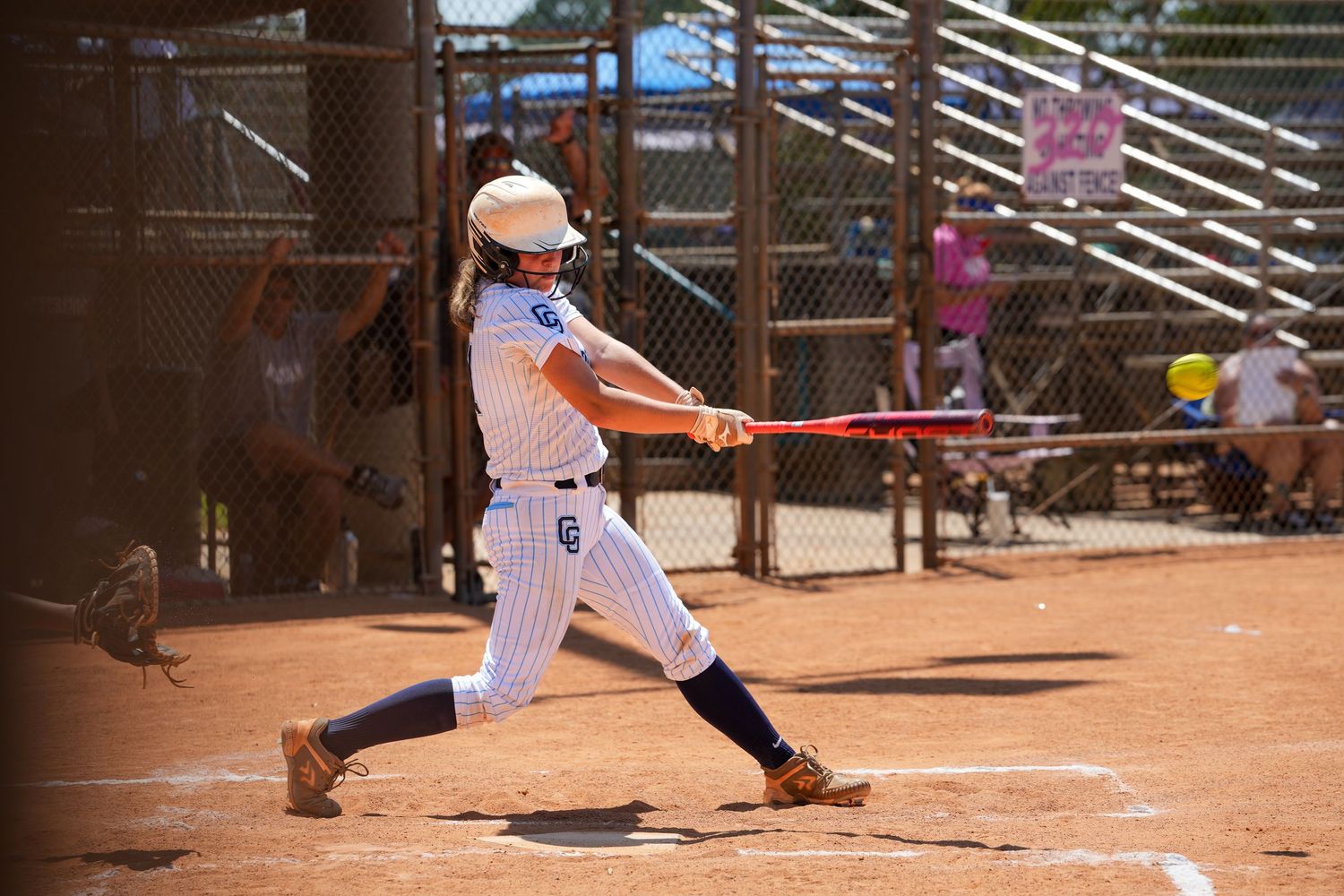 Baseball player in pinstripe uniform swinging bat during game on dirt field.