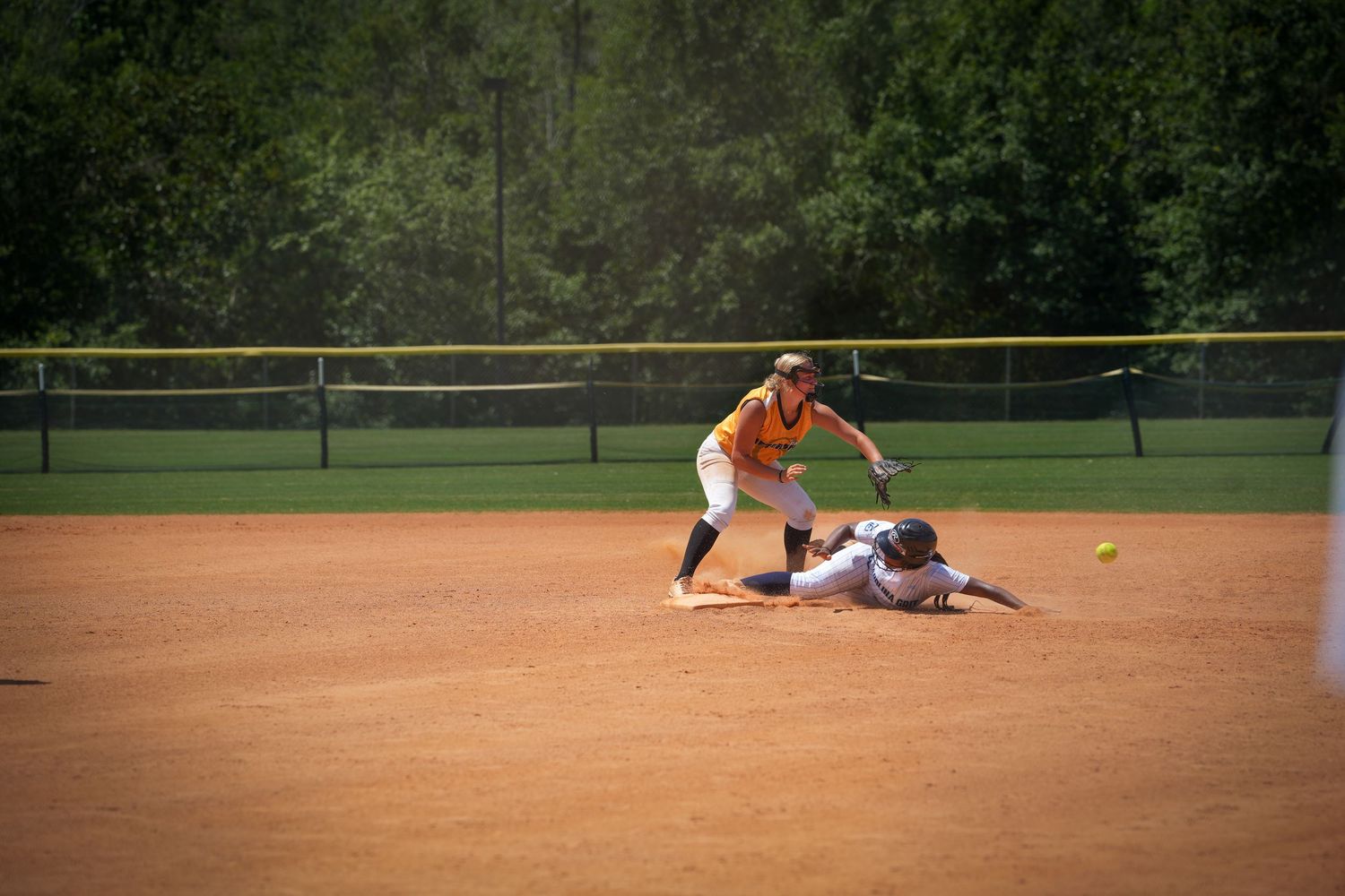 Action shot of baseball players during a sliding play at base on dirt infield.