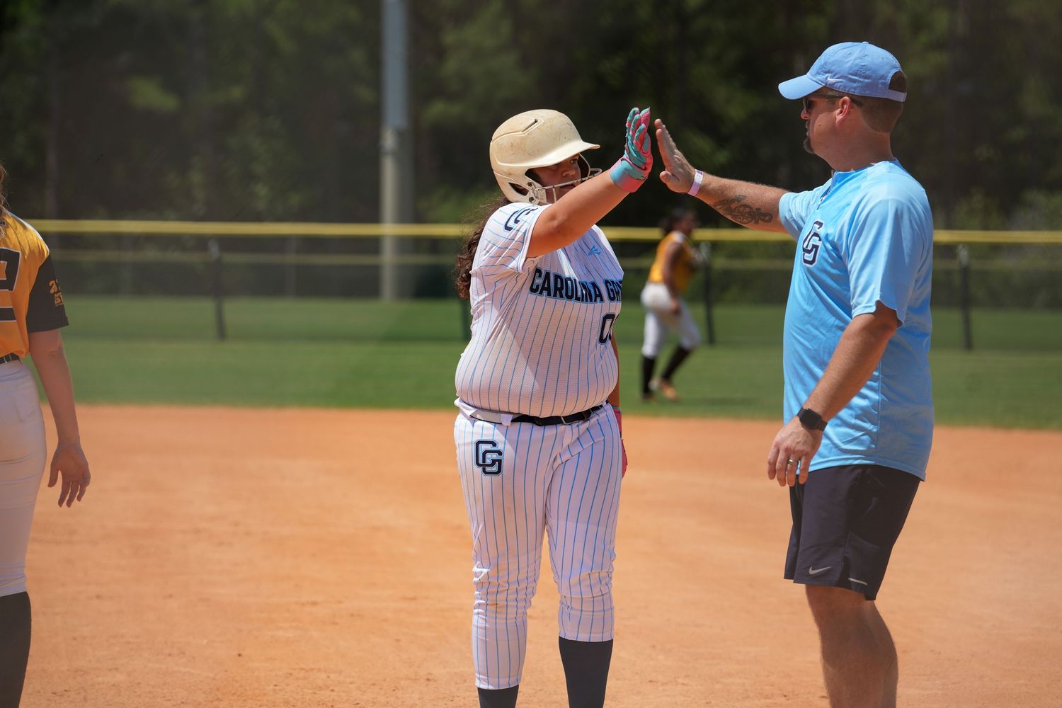 Baseball player in pinstripe uniform giving high five to coach on sunny field during game.