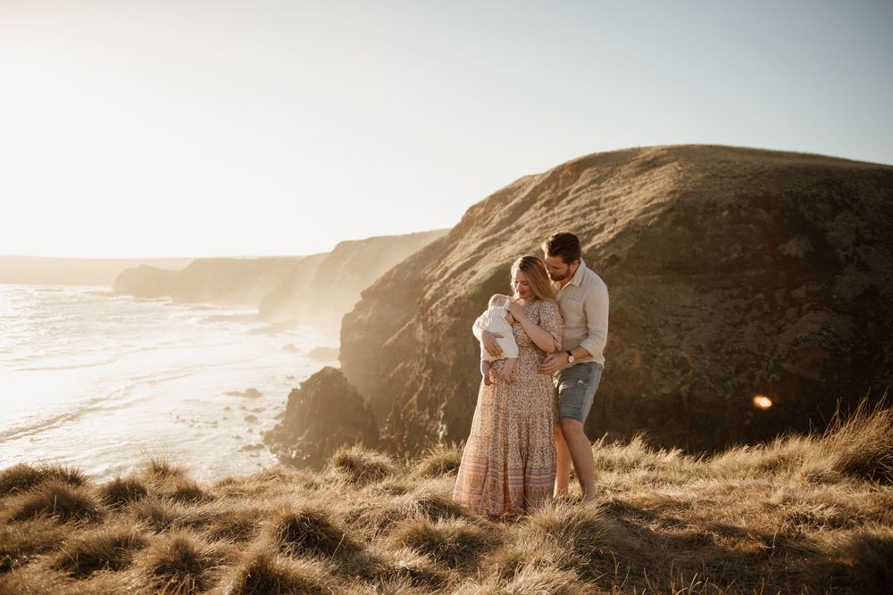A romantic couple embraces on a scenic coastal cliff at sunset with ocean waves crashing below.
