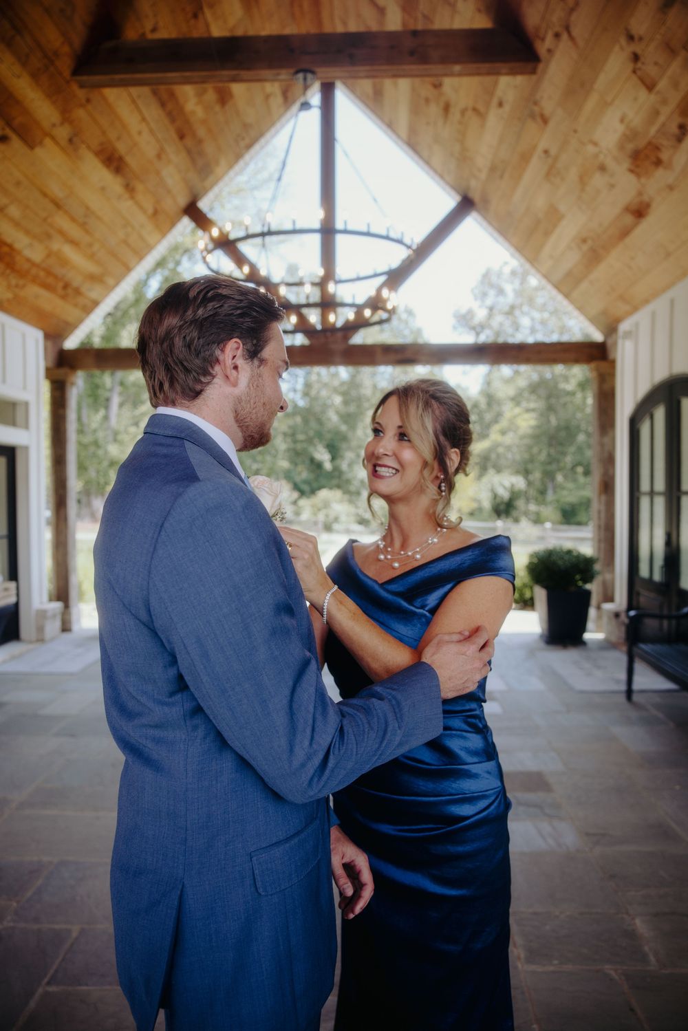 Groom in blue suit shares tender moment with woman in navy off-shoulder gown under wooden venue ceiling.